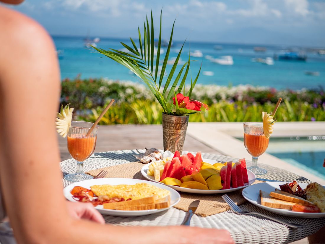 A tropical breakfast of fruit, eggs and juice beside a pool overlooking the sea