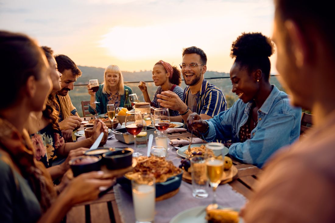 Friends laughing over dinner at a long table on a terrace at sunset