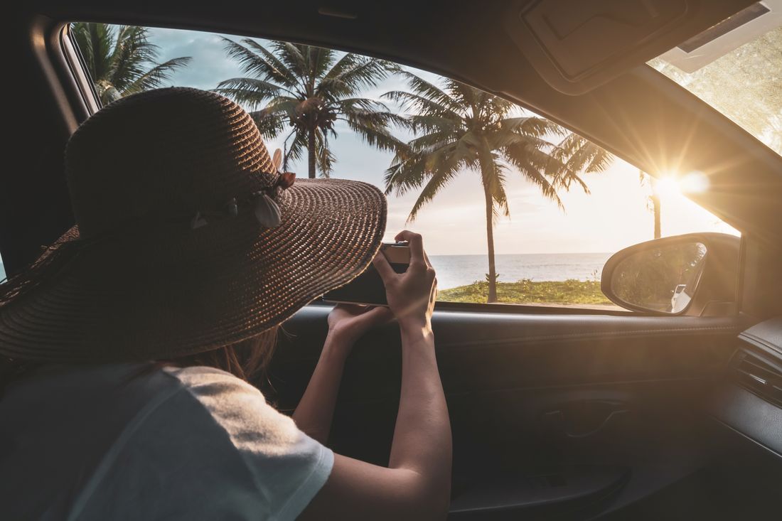 A traveller taking photos from a car window on a palm-lined coastal road