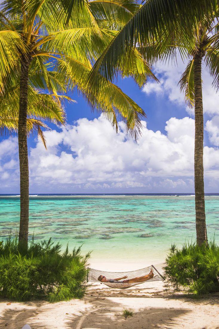 A traveller relaxing in a hammock between palm trees on a white sand beach